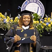 Shaquita Callier dressed in cap and gown, holding her diploma as confetti falls down at her SNHU Commencement cermeony