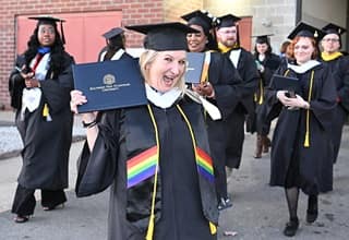 An SNHU graduate holding a diploma outside of the SNHU Arena, after the end of a Commencement ceremony.
