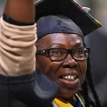 An SNHU graduate with a cap and gown, raising their arm.