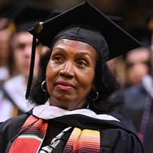 An SNHU graduate wearing a cap and gown, listening to the Commencement ceremony.