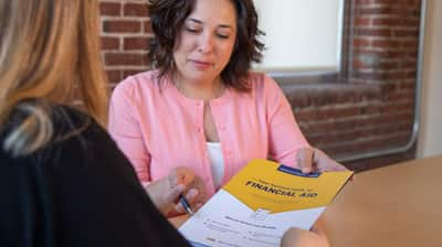 Two people at a desk discussing financial aid documents.