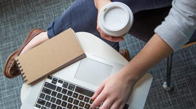 Person holding a cup of coffee while working on their laptop.