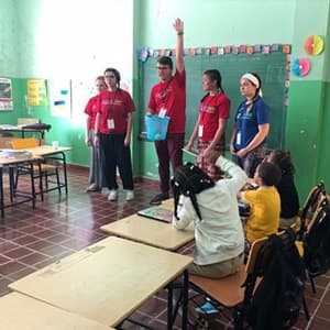 5 young adults in front of a classroom in the Dominican Republic teaching young children English.