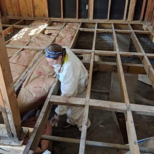 A woman standing between floor joists installing insulation in a partially-built North Carolina home.