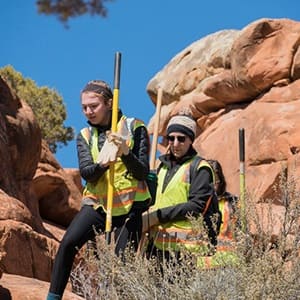 A man and woman in yellow safety vests working to restore a trail in Arches National Park.