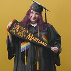 Amber Bownan, an associate in liberal arts and bachelor's in general studies graduate from SNHU holding a Maryland state flag and wearing her cap and gown in front of a yellow background.