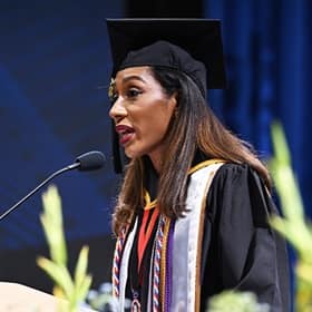Annais Roman, a student speaker at SNHU's 2025 Fall Commencement, at a podium, wearing a cap and gown.