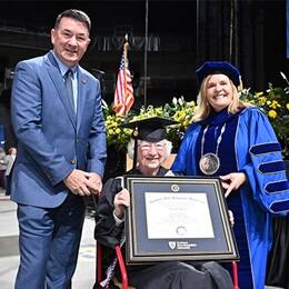 Annette Roberge holding her framed diploma between her son and SNHU President Lisa Marsh Ryerson.