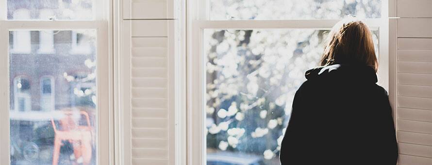 A person leaning against a window frame, considering the barriers to mental health awareness and treatment.