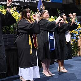 Three of six graduates from SNHU's campus performing the national anthem in American Sign Language, dressed in their graduation caps and gowns.