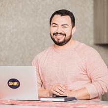 Jesús Suárez smiling while sitting behind a SNHU laptop