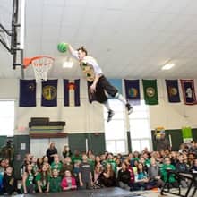 Celtics mascot Lucky soaring through the air about to dunk a green basketball during a pep rally at Green Acres Elementary School.