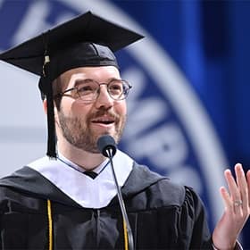 Jack Kohaut, a student speaker at SNHU's 2025 Fall Commencement, at a podium, wearing a cap and gown.