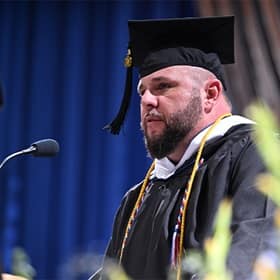 John Nolan, a student speaker at SNHU's 2025 Fall Commencement, at a podium, wearing a cap and gown.