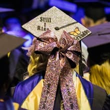 An SNHU graduate wearing a sparkly mortarboard with a pink bow and the words Still I Rise