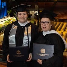 Susan Lasala and Jennifer Gardner in their cap and gown and holding SNHU degrees.
