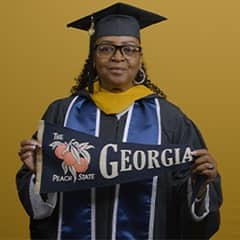 Cynthia Preston dressed in a graduation cap and gown after earning her bachelor's in marketing at SNHU in 2026 holding a Georgia state flag.