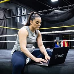 Deonna Purrazzo working on her SNHU school work sitting in a wrestling gym.