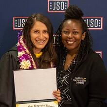 Diana Tafoya Sanchez with her gown on and a Hawaiian lei holding her diploma standing with SNHU Regional Manager of Military Alliances Victoria White