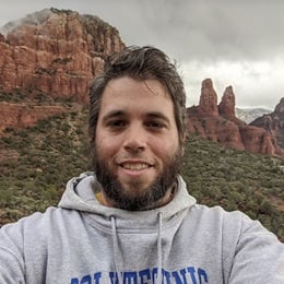 Dr. Jonathan Davis, an instructor of SNHU’s bachelor’s in geosciences program, wearing a grey hooded sweatshirt in from of red rock formations.