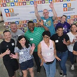 Volunteers smiling and waving in front of a community organization banner.