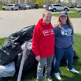 Two volunteers standing on a grassy area beside large bags of collected trash.