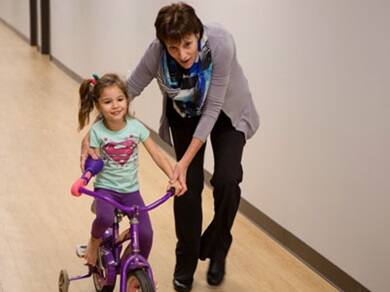 Little girl riding a bike with the help of a family member and a prosthetic attachment created by SNHU engineering students