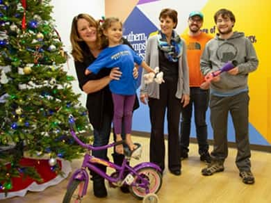 Little girl standing on her bike with a prosthetic attachment alongside two family members and two SNHU students.