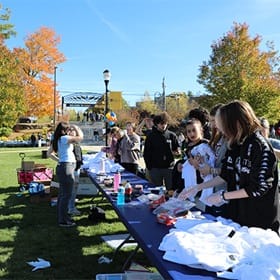 A long row of folding tables holding tie dye supplies and people gathered around it.