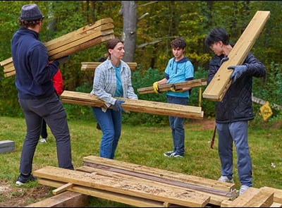 Four people carrying wood as they complete a service project in the SNHU Arboretum during 2023 Homecoming