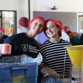Volunteers packaging meals wearing red hair nets at the Rise Against Hunger service project