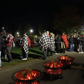 A group of people gathered on a lawn with fire pits before Homecoming fireworks.