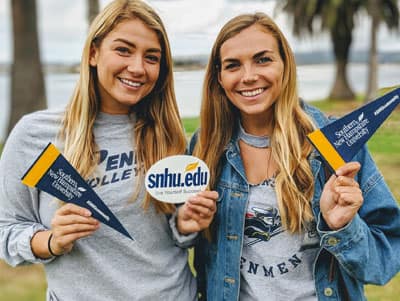 Two women at SNHU homecoming holding SNHU sticker and pennants.