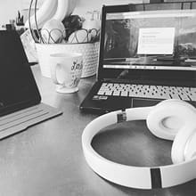A laptop, headphones and mug of coffee on a kitchen table.