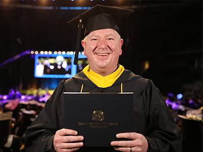 Justin Smith, who earned his SNHU degree in 2024, wearing his cap and gown and holding his diploma.