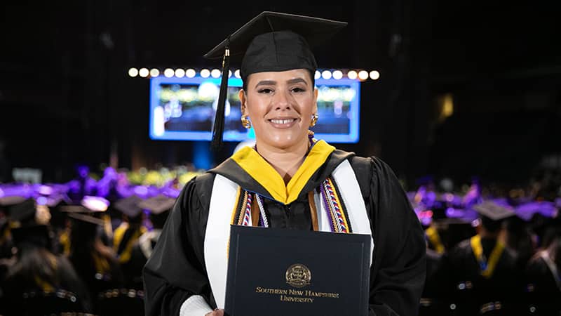 Priscilla Vega, who earned her online bachelor's in business administration from SNHU in 2024, wearing her cap and gown and holding her diploma.