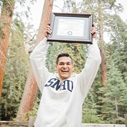 Juan Munoz '22 '24MBA, bachelor's in general studies and Master of Business Administration (MBA) from SNHU holding his diploma above his head. 