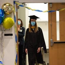 Katie Smith wearing graduation regalia and a mask, entering the auditorium to receive her diploma. 