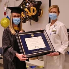 Katie Smith, left, wearing graduation regalia, and Karen Clements, right, both in masks and holding a framed SNHU diploma.
