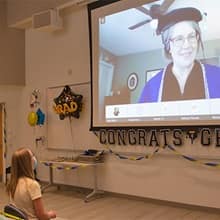 Katie Smith sitting in an DHMC auditorium, listening to Dr. Kimberly Gibbons deliver remarks in a video chat. 