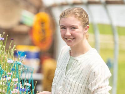 Kayla Stoll, a student in SNHU's online bachelor's in environmental science program, wearing a white blouse and standing in greenhouse.