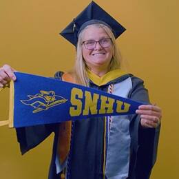 Kelly Pilotte '25, SNHU graduate with a bachelor's in business administration with a concentration in nonprofit management, holding an SNHU pennant.