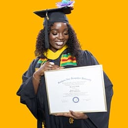 Kendreka Griffin, a 2024 SNHU graduate who earned her bachelor's in business administration, wearing her cap and gown in front of a yellow background, looking down, smiling at her diploma.