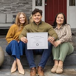 Kevin Bucardo '25MBA, MBA with a concentration in Finance graduate from SNHU, holding his diploma surrounded by family.