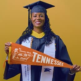 Kyla Johnson-Curtis, a 2025 SNHU grad who earn her bachelor's in operations management with a concentration in logistics and transportation holding a Tennessee flag in front of a yellow background.