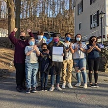 The Gaughan family wearing masks and cheering for Laura Gaughan, center, who is dressed in graduation cap and gown and holding her diploma. 