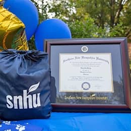 Loretta Gray's SNHU diploma beside an SNHU drawstring bag and balloons.
