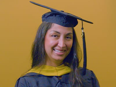 SNHU graduate, Luciana Henderson '25G, wearing cap and gown while holding her diploma.