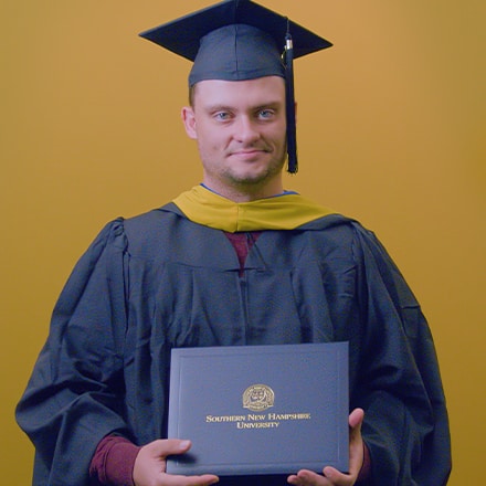Luke Blaeser, a 2025 SNHU grad who earned his master's in healthcare administration holding his diploma in front of a yellow background.