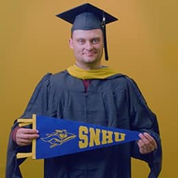 Luke Blaeser, a 2025 SNHU grad who earned his master's in healthcare administration holding a SNHU flag in front of a yellow background.